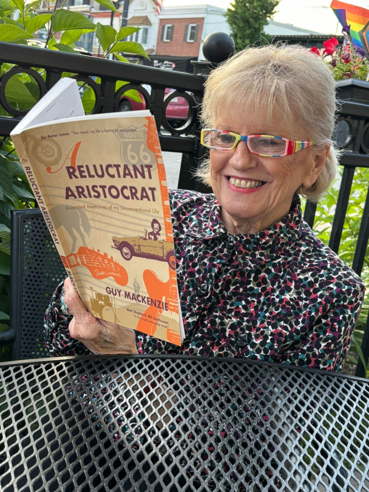 Photo of Joan Gracie with a copy of the book 'A Reluctant Aristocrat' by Guy Mackenzie.